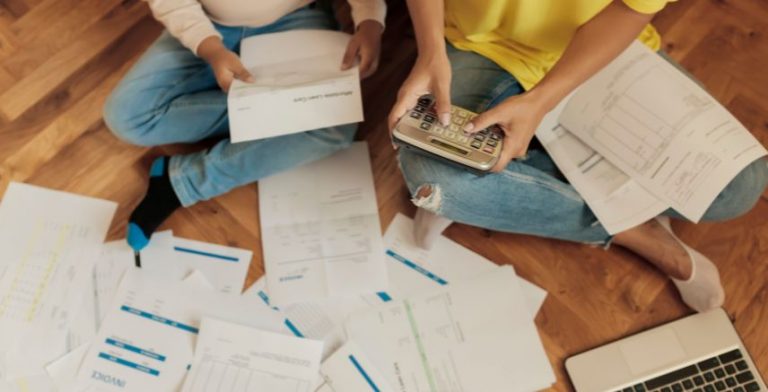 Two people sitting on the floor surrounded by bills. They are holding a calculator.